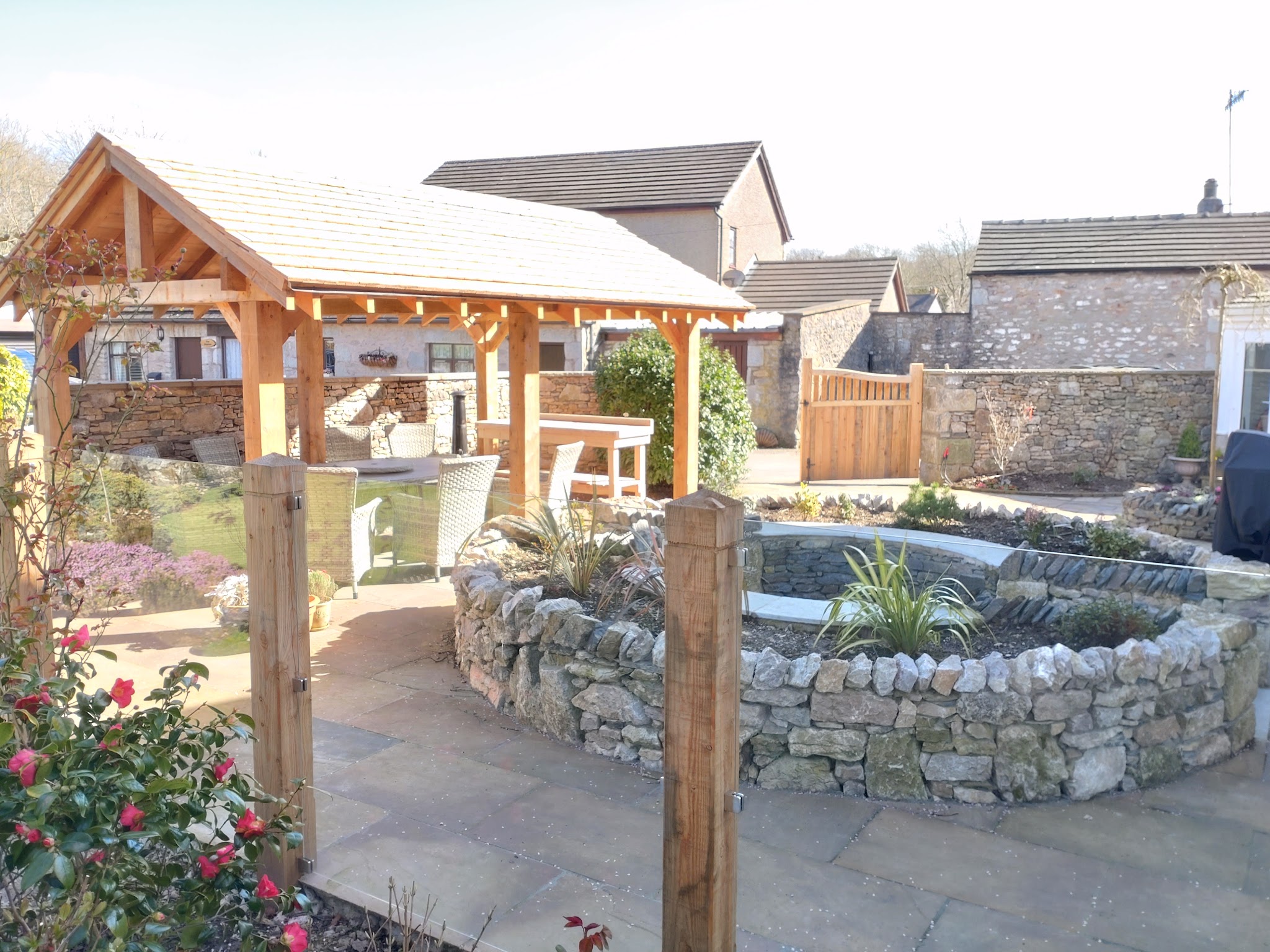 Oak-framed pergola over a paved courtyard with a round drystone raised pond