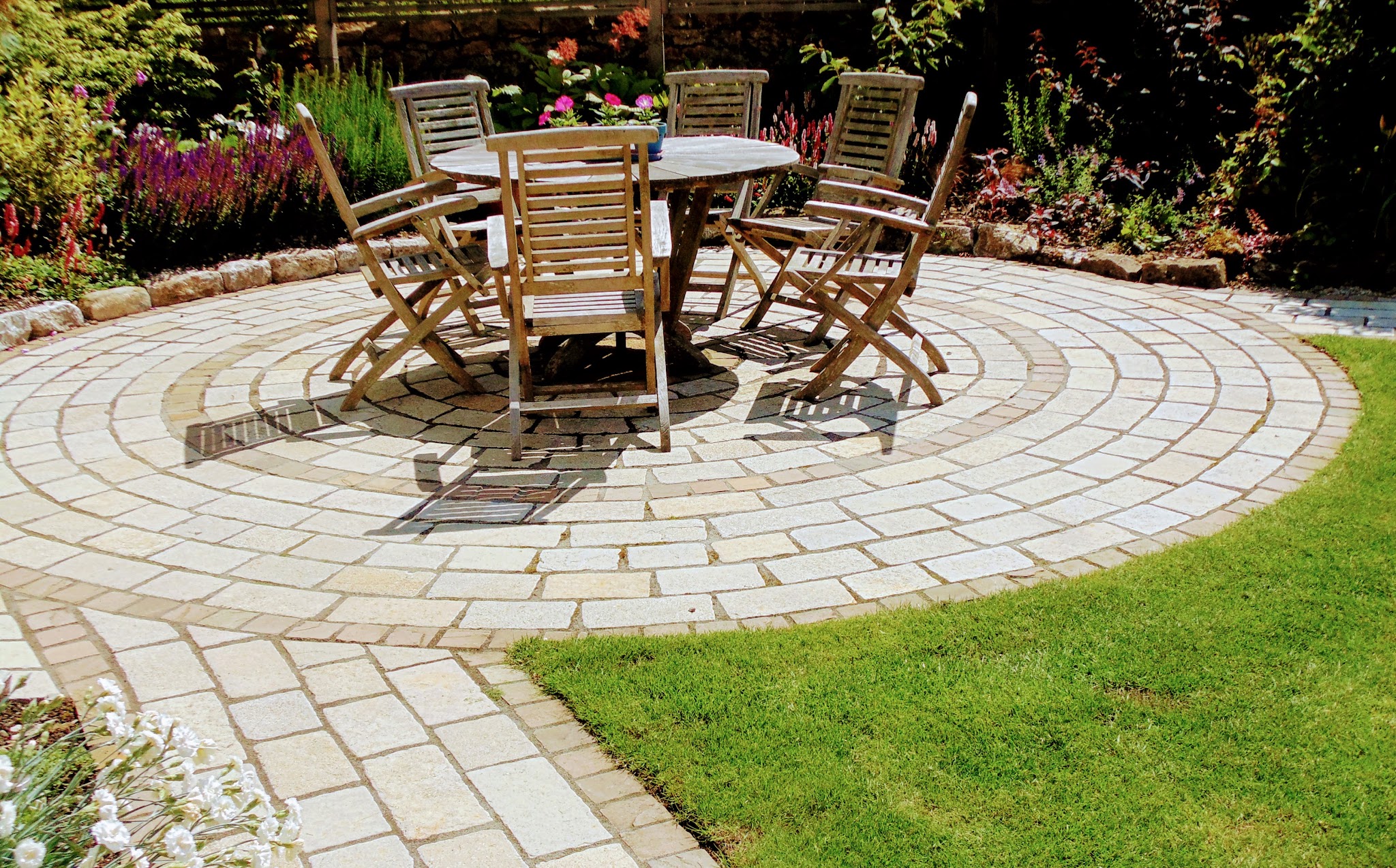 Circular setts patio with a table and chairs, a path and lawn