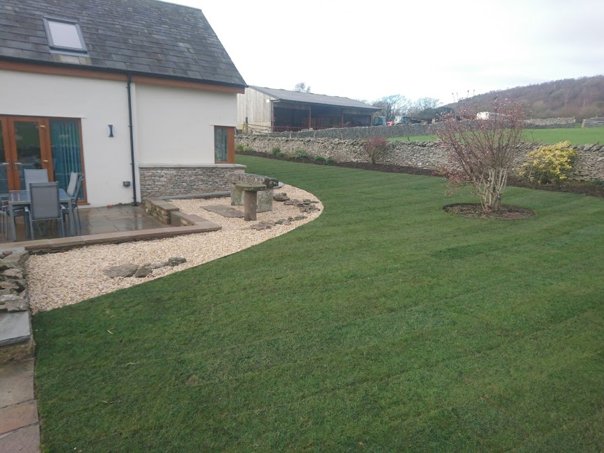 New lawn with a curved gravel edge and a patio beside a barn conversion, hills beyond