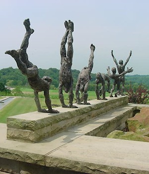 A row of bronze figures doing handstands along a stone wall