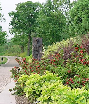 A carved figure beside a border of red and lime planting