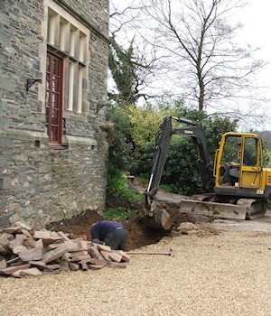 A mini excavator digging beside the house wall