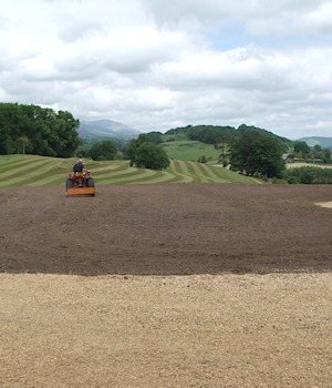 Levelled ground with a tractor, fells beyond